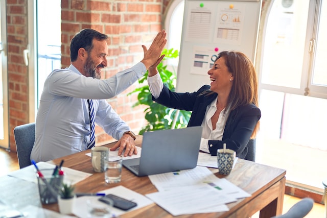 Two people working at a table together, they are high fiving